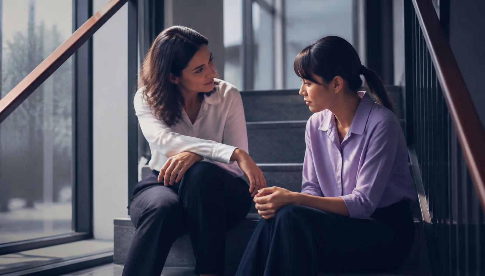 Two colleagues sitting together in a quiet space having a caring, private conversation